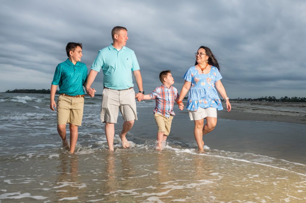 Family joyfully walking along Tybee's sandy shores, capturing the warmth of sunset and the essence of their beach getaway. Professional vacation portrait by [Your Name], blending natural beauty with skilled photography to create timeless memories on Tybee Island.